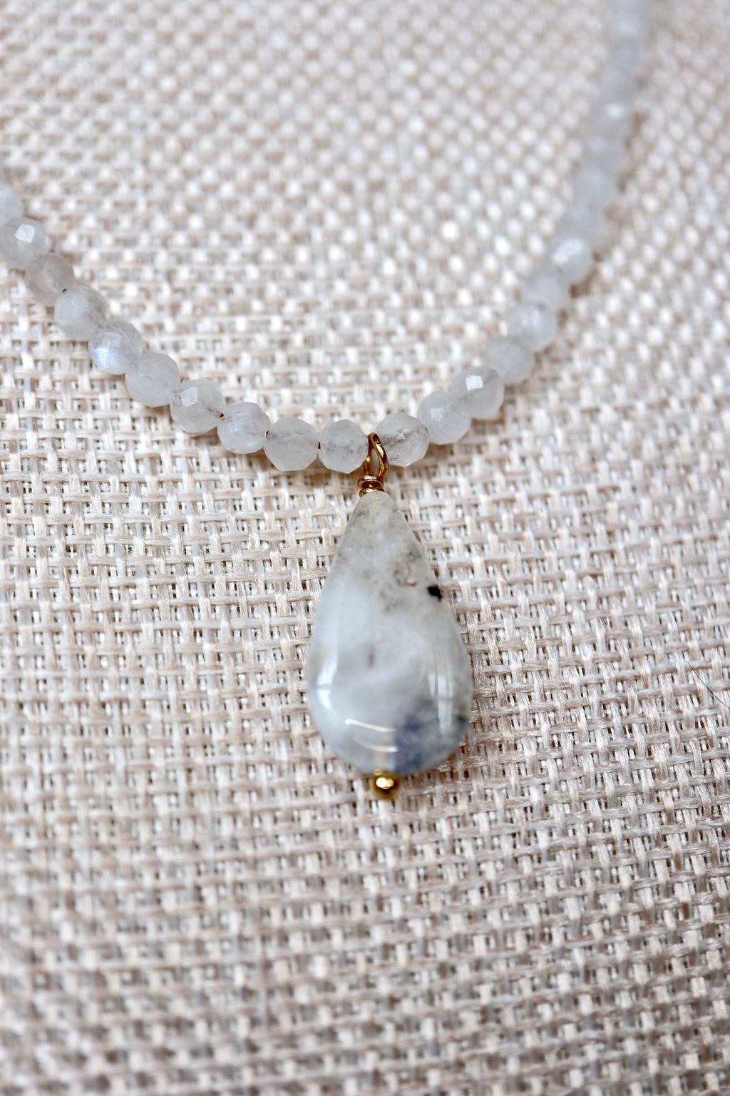 Close-up of the moonstone teardrop pendant and rainbow moonstone rondelles on the Snow necklace by Auréad Designs, showing the stone's translucent white color and natural inclusions