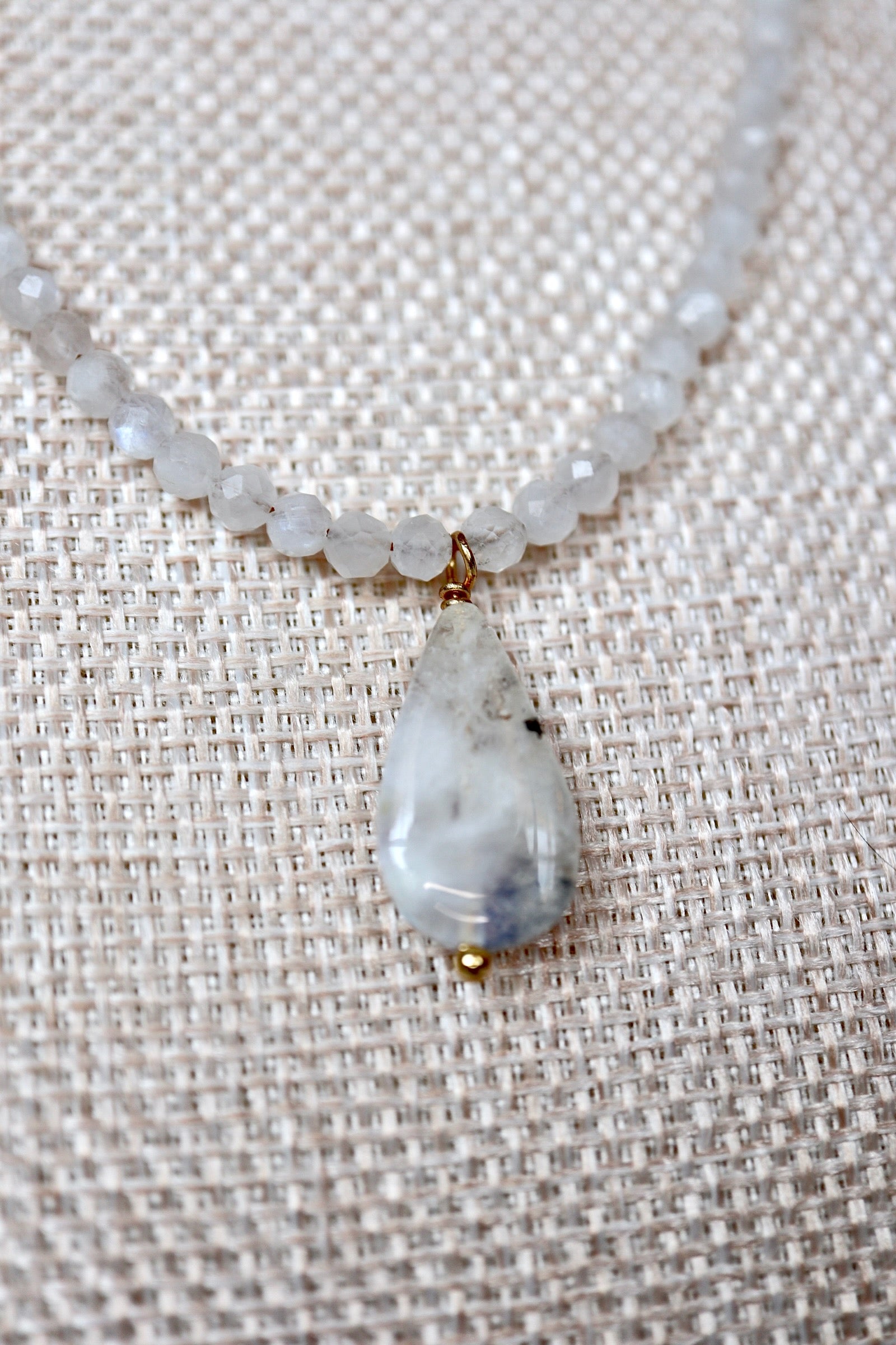 Close-up of the moonstone teardrop pendant and rainbow moonstone rondelles on the Snow necklace by Auréad Designs, showing the stone's translucent white color and natural inclusions