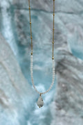 Snow necklace by Auréad Designs held against the blue ice face of the Athabasca Glacier, with rainbow moonstone rondelles, gold satellite chain, and moonstone teardrop pendant