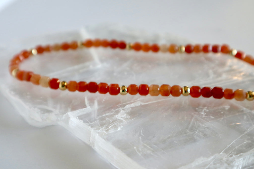 Close-up of the Solara necklace showing vibrant orange aventurine beads with gold spacer beads laying on a selenite slab