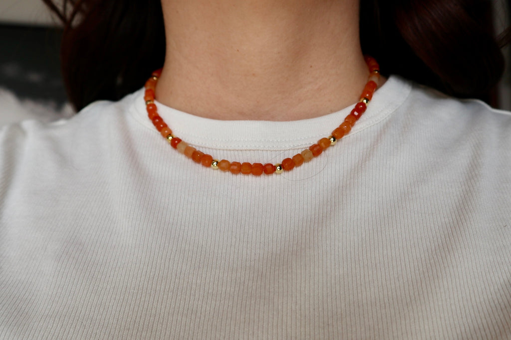 Close-up of the Solara necklace resting at the collarbone, highlighting the warm luminous tones of orange aventurine beads and gold-filled accents
