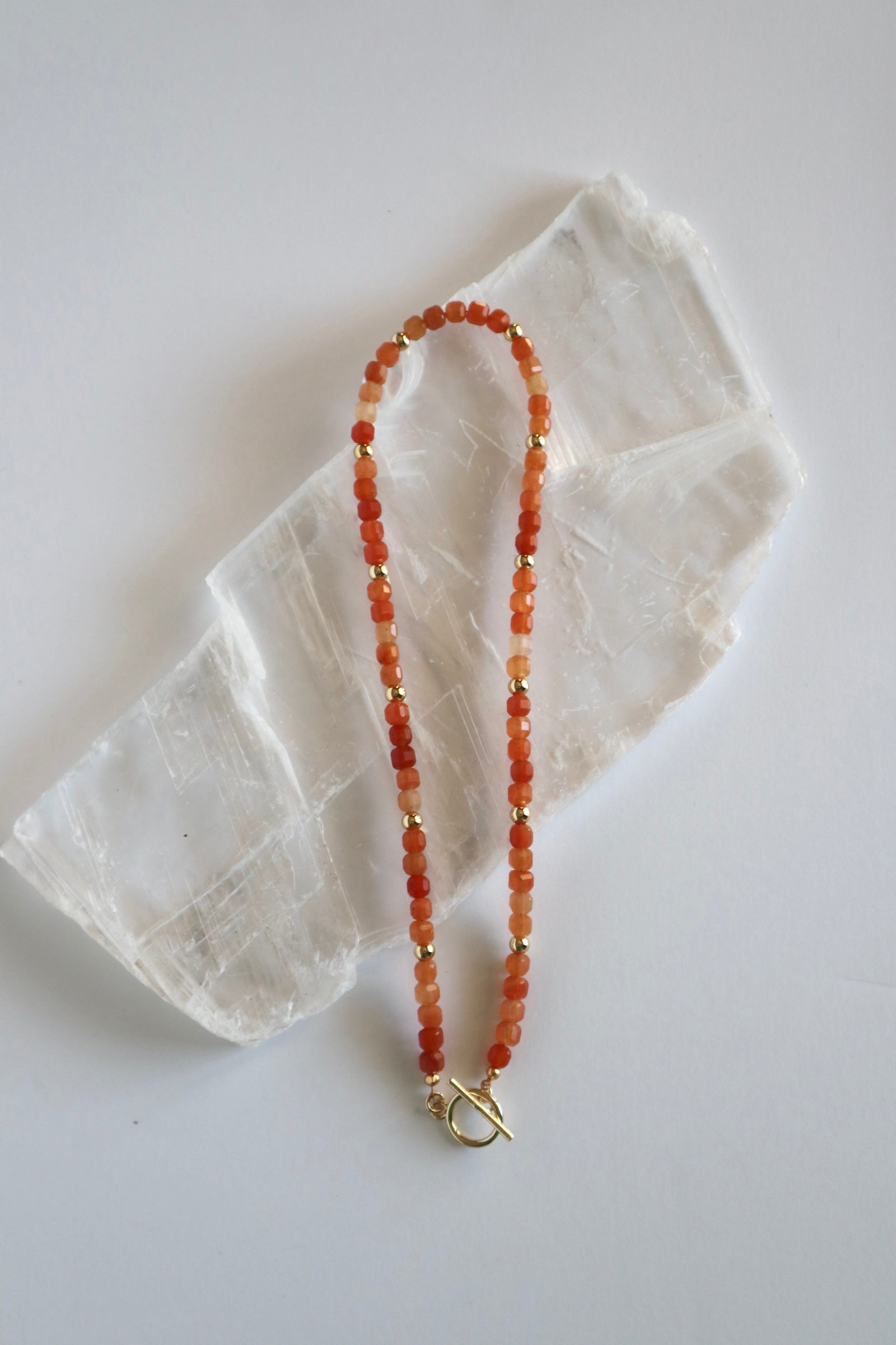 Solara necklace by Auréad Designs, featuring orange aventurine gemstone beads and gold-filled toggle clasp, laid flat on a white selenite slab