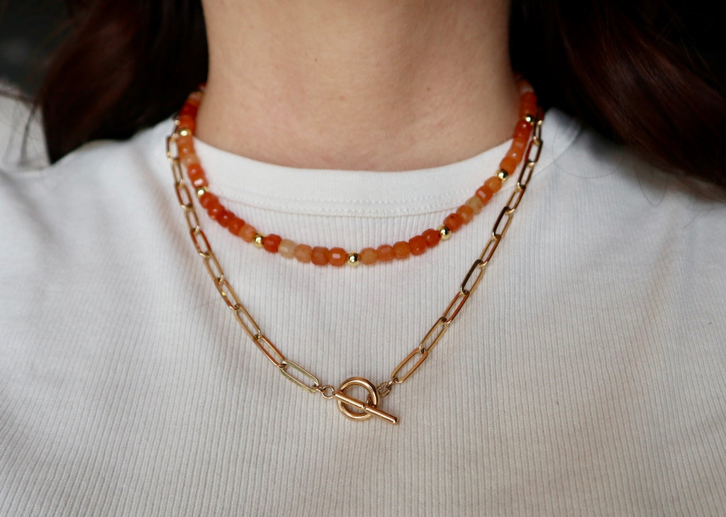 Solara necklace by Auréad Designs layered with a delicate gold chain, worn on model to show a curated necklace stack with orange aventurine as the focal piece