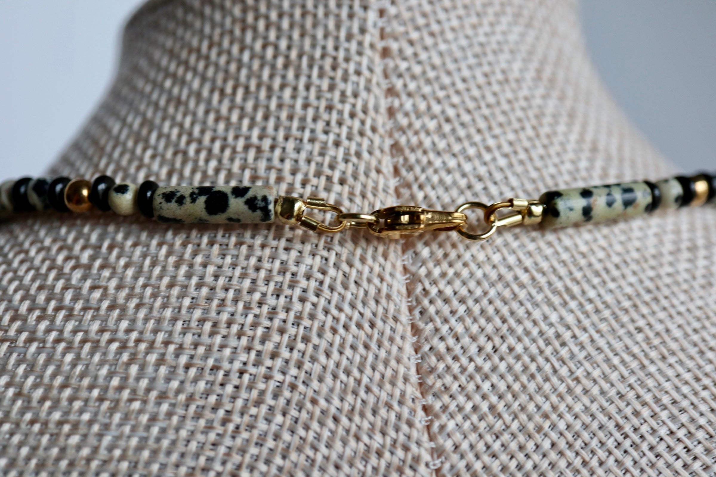 Close-up of the Sorren necklace on a linen bust form, highlighting the lobster clasp, the natural speckled and smoky tones of dalmatian jasper, and ice obsidian beads