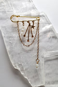 Stellune pin brooch by Auréad Designs, featuring moonstone beads, gold stainless steel charms, and draped gold chains, laid flat on a white selenite crystal