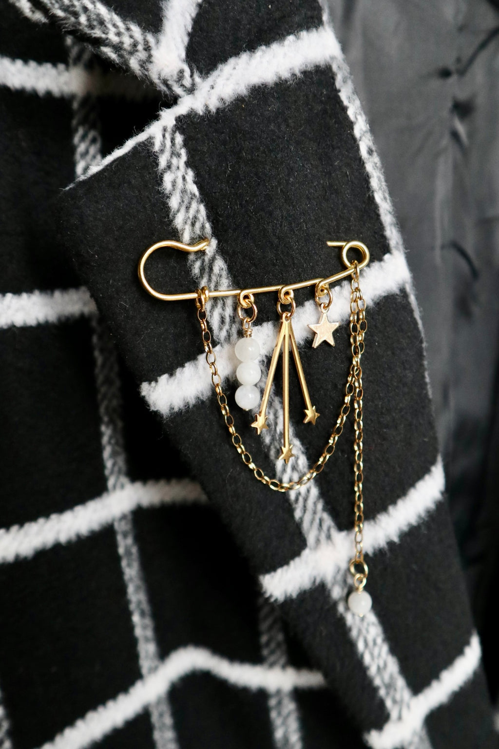 Stellune brooch by Auréad Designs pinned to a dark plaid jacket, showcasing gold stainless steel charms and cascading chains against a textured fabric