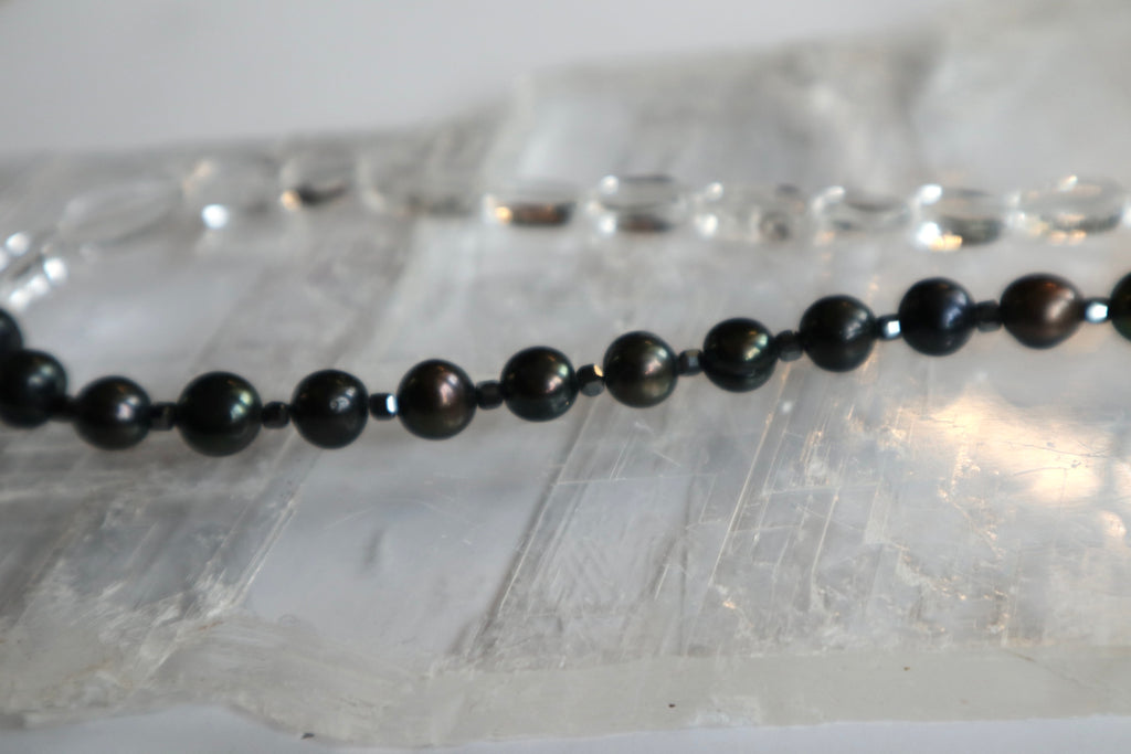 Close-up of the Tashira necklace showing the contrast between clear quartz, iridescent black peacock freshwater pearls, and hematite spacer beads