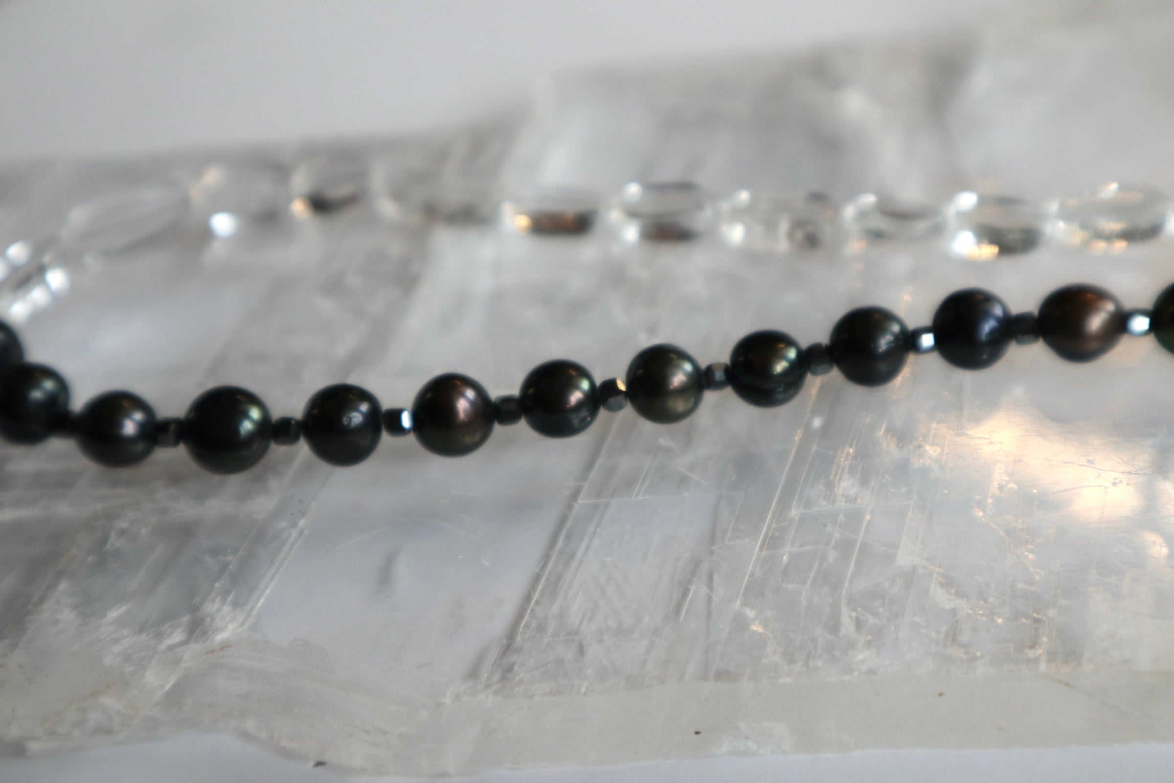 Close-up of the Tashira necklace showing the contrast between clear quartz, iridescent black peacock freshwater pearls, and hematite spacer beads