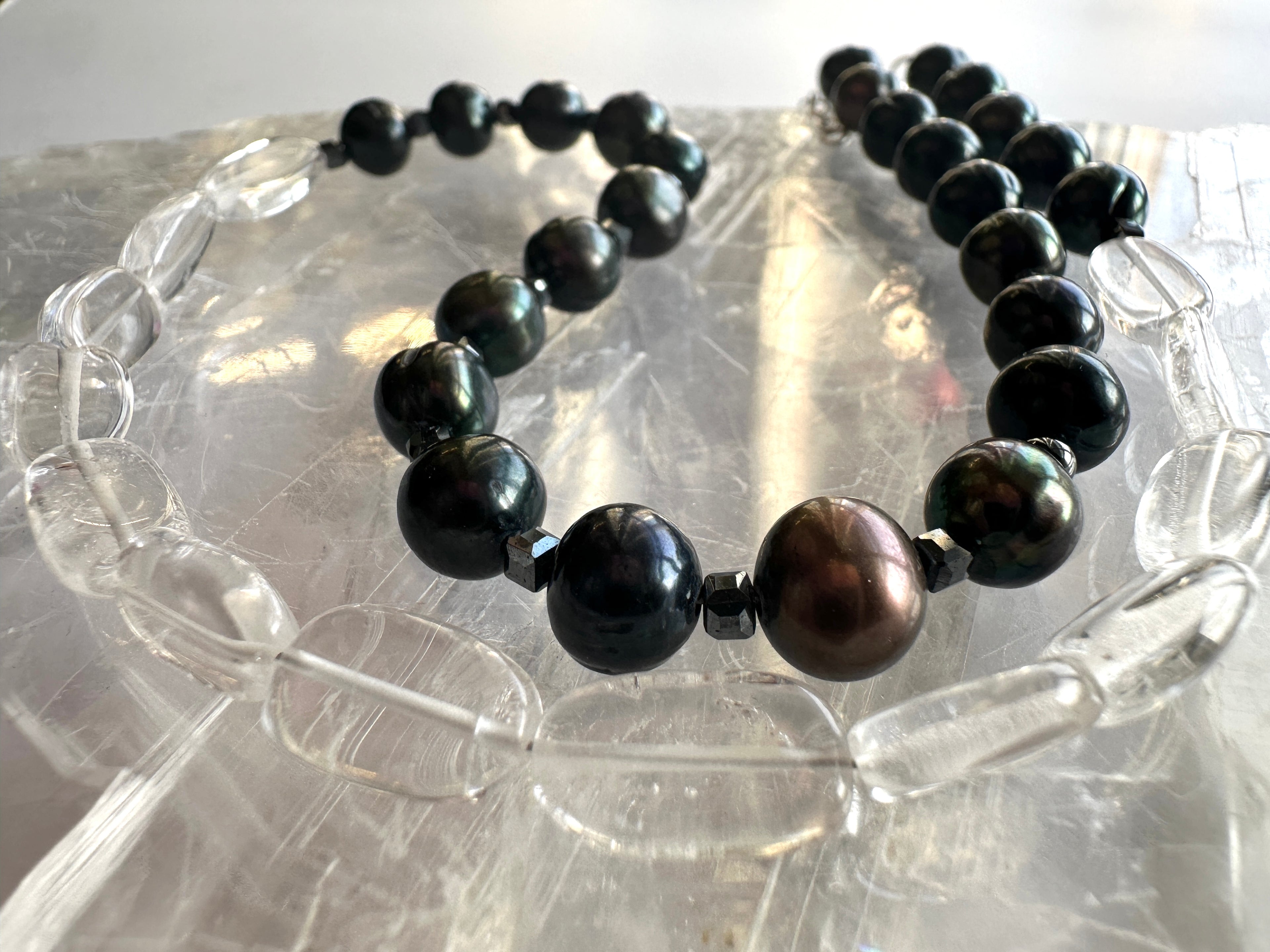 Tashira necklace by Auréad Designs displayed on a light surface, showcasing the full strand of clear quartz, black peacock freshwater pearls, and hematite spacer beads