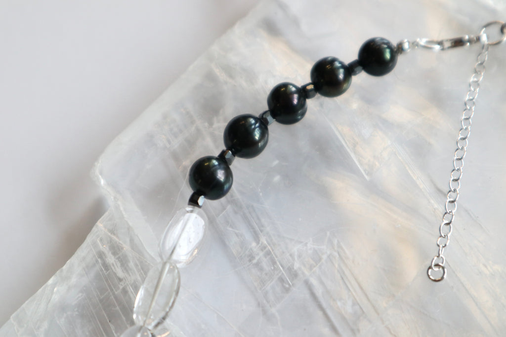 Detail shot of the Tashira necklace sterling silver clasp and extender chain, with clear quartz and black peacock pearl beads visible along the strand