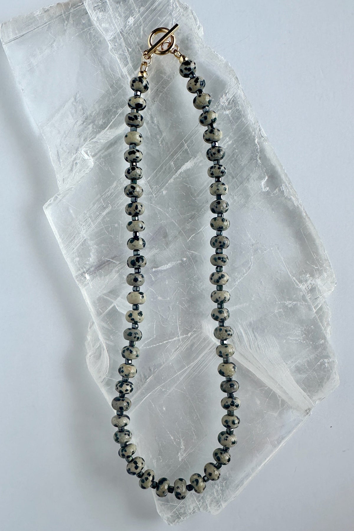 Tessere Dalmatian jasper and hematite beaded necklace by Auréad Designs on white selenite slab
