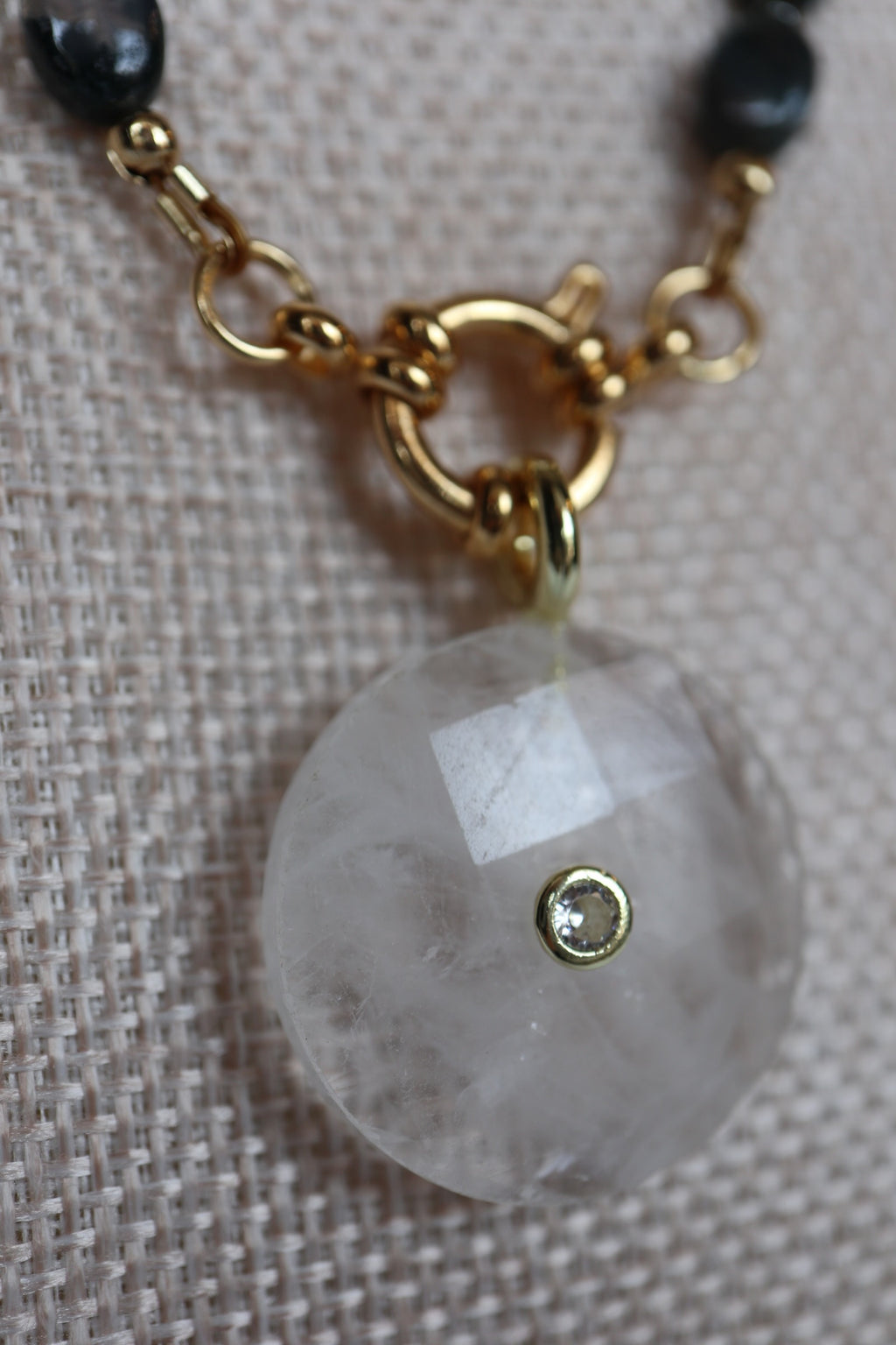 Close-up of the clear quartz donut pendant and gold ring clasp on the Trail necklace by Auréad Designs, showing the pendant's faceted surface and decorative clasp detail
