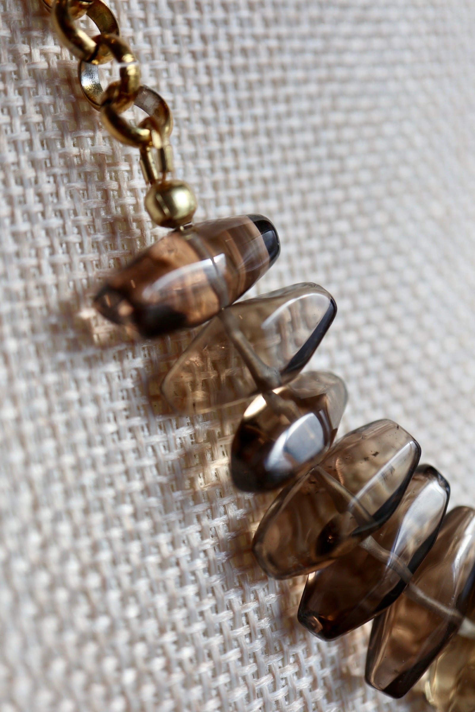Close-up of the Umbra necklace showing faceted smoky quartz drops suspended from a gold stainless steel rolo chain