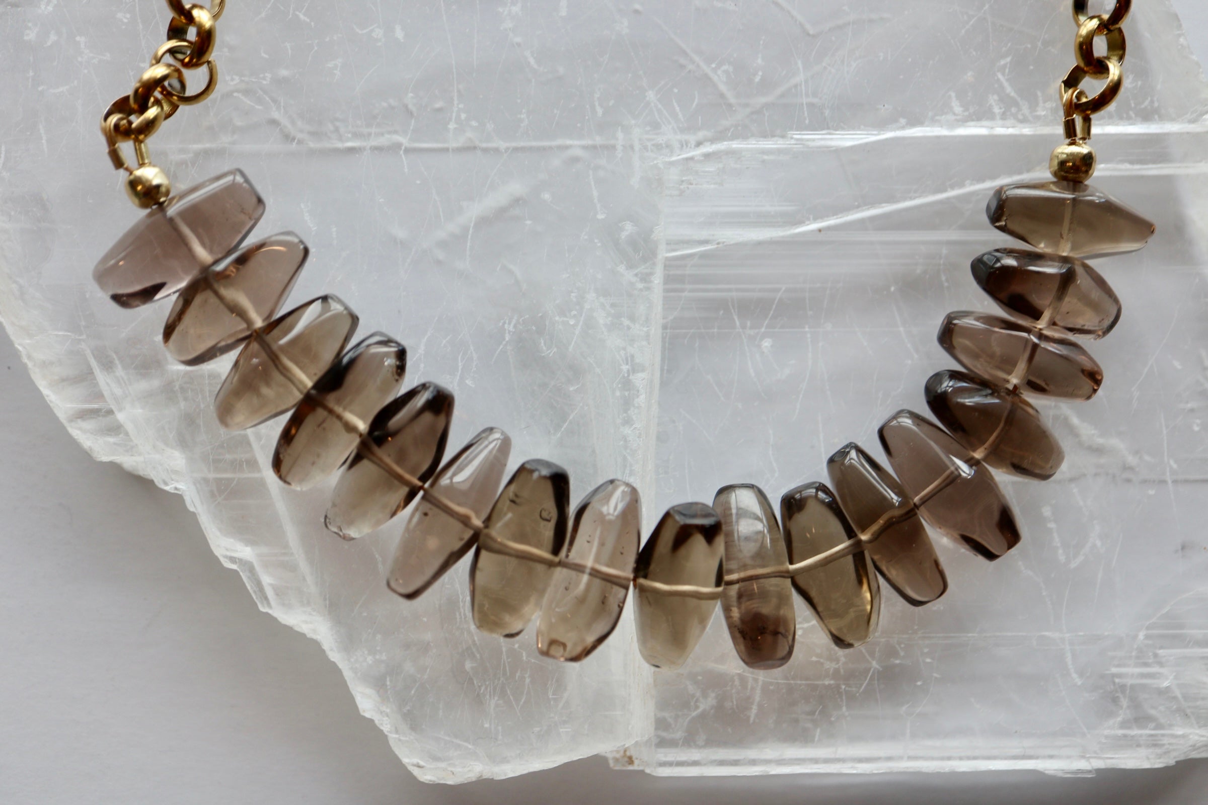 Umbra smoky quartz and gold rolo chain necklace displayed on a selenite slab showing the full beaded drop arrangement