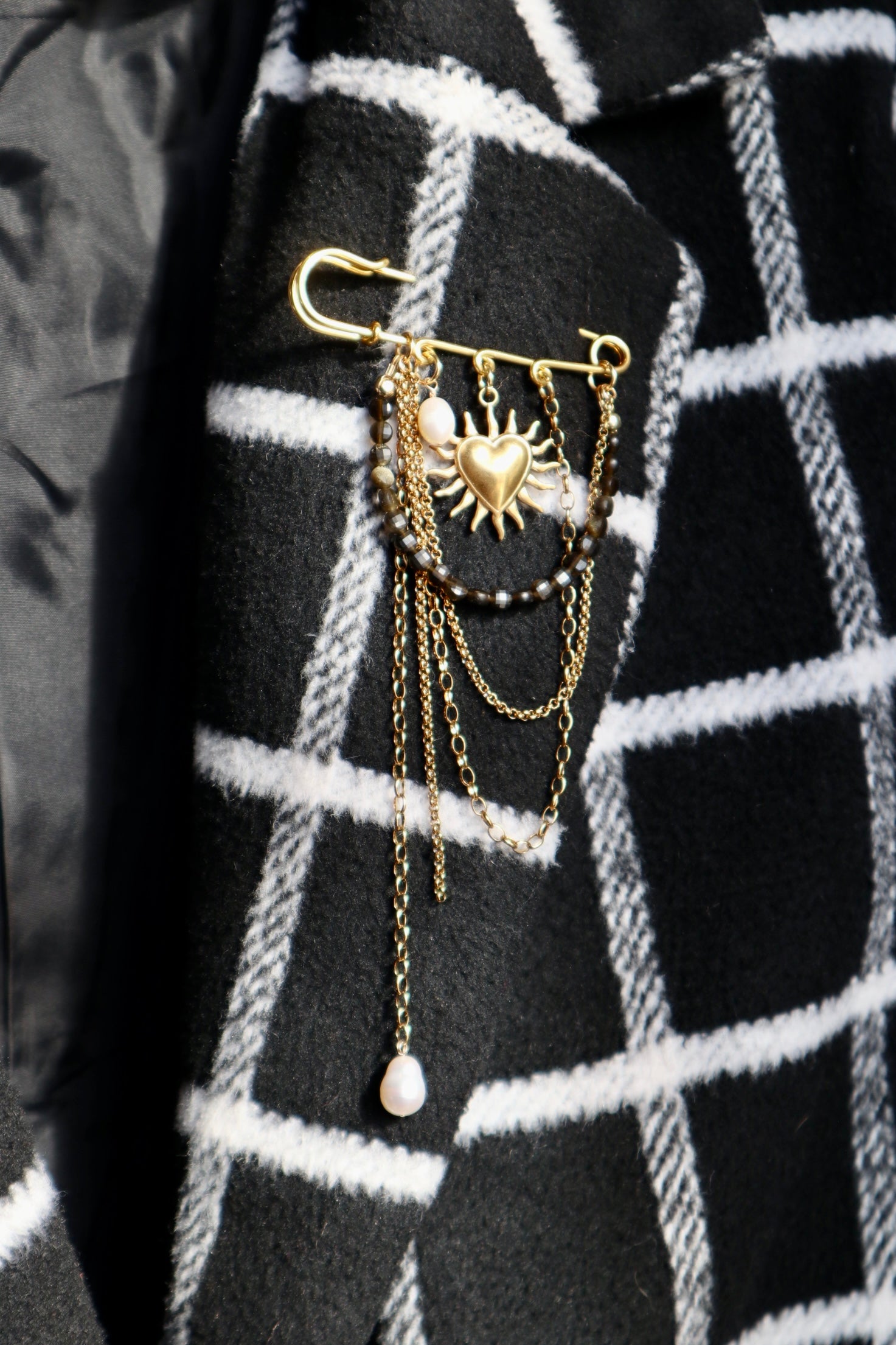 Velora brooch by Auréad Designs pinned to a dark plaid jacket, styled to show the contrast of gold chains and obsidian against a textured fabric