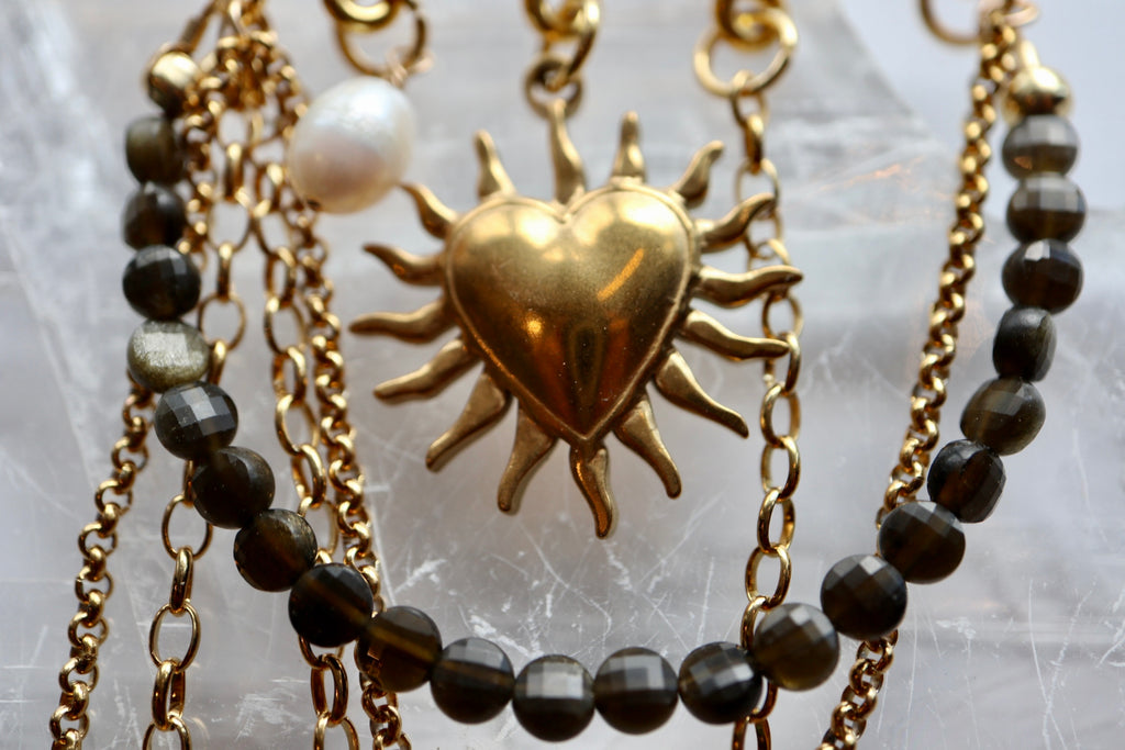 Detailed close-up of the Velora brooch pinned to fabric, highlighting the gold sheen obsidian stone, freshwater pearl, and layered chain drape