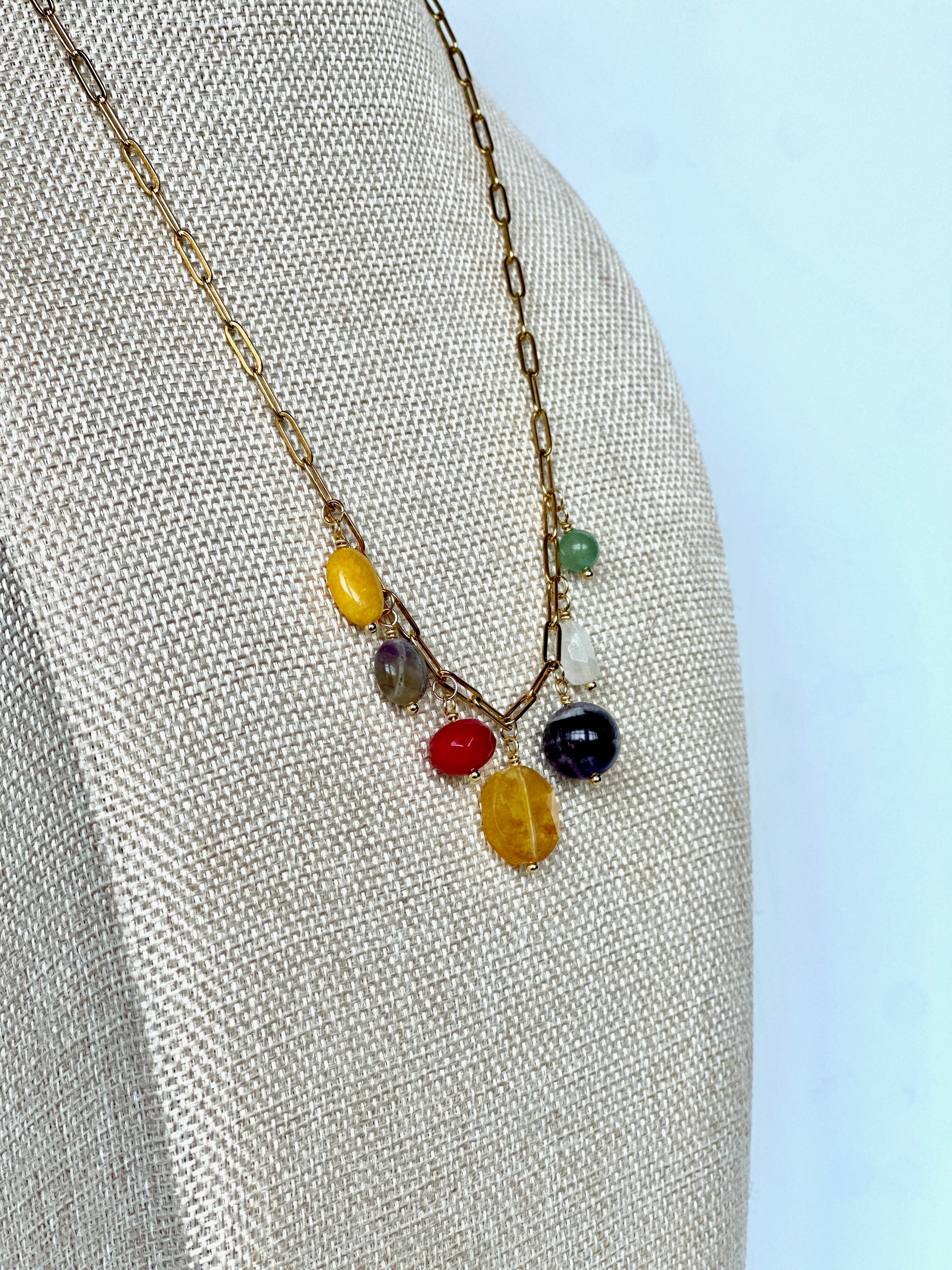 Wildflower necklace by Auréad Designs on a linen bust, angled view, showing the cluster of colorful gemstone drops including green aventurine, amethyst, yellow jade, golden healer quartz, rainbow moonstone, fuschia-dyed agate, and freshwater pearl