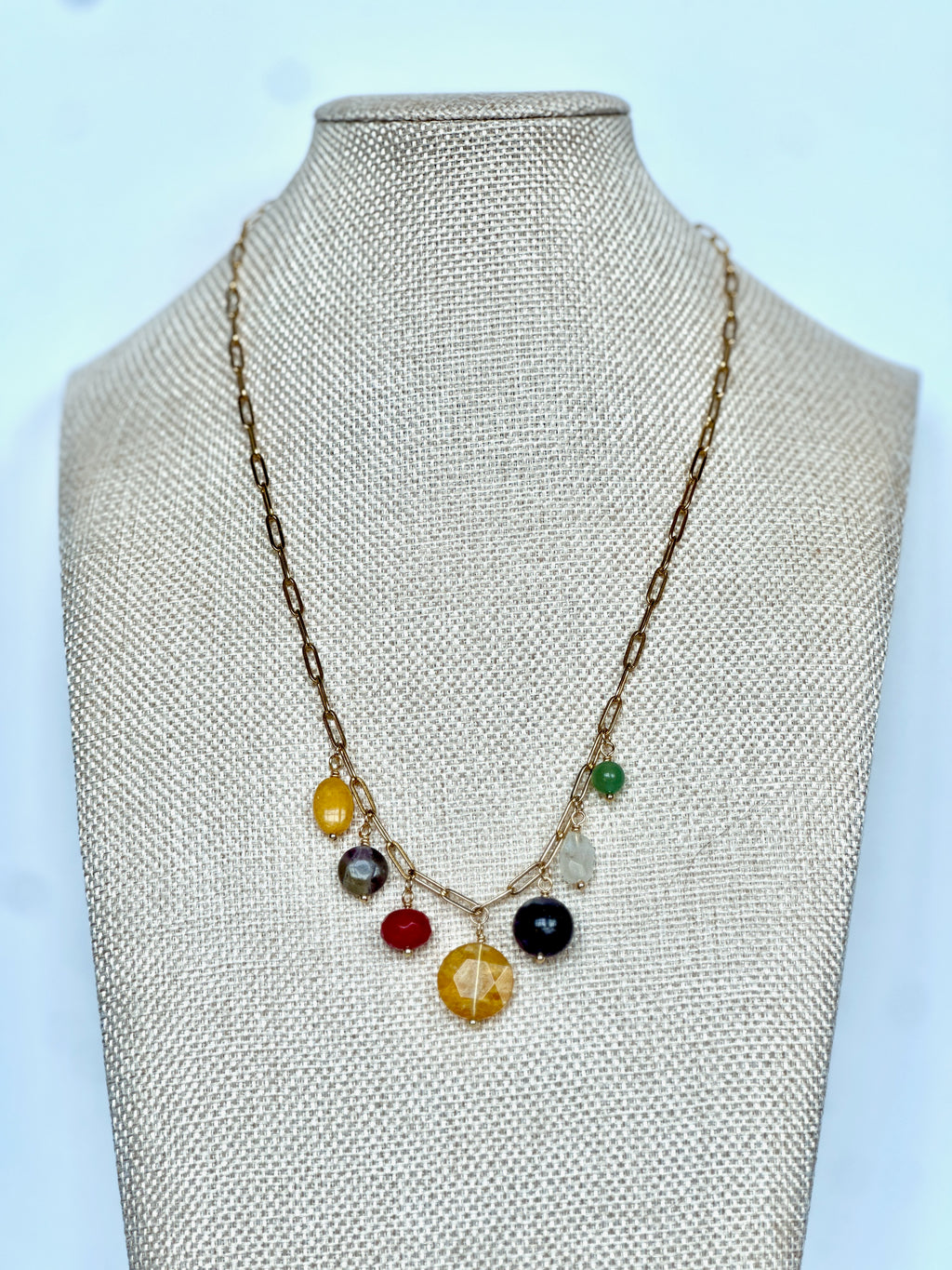 Wildflower necklace by Auréad Designs on a linen bust, front view, showing the full arrangement of seven colorful gemstone drops on a gold paperclip chain