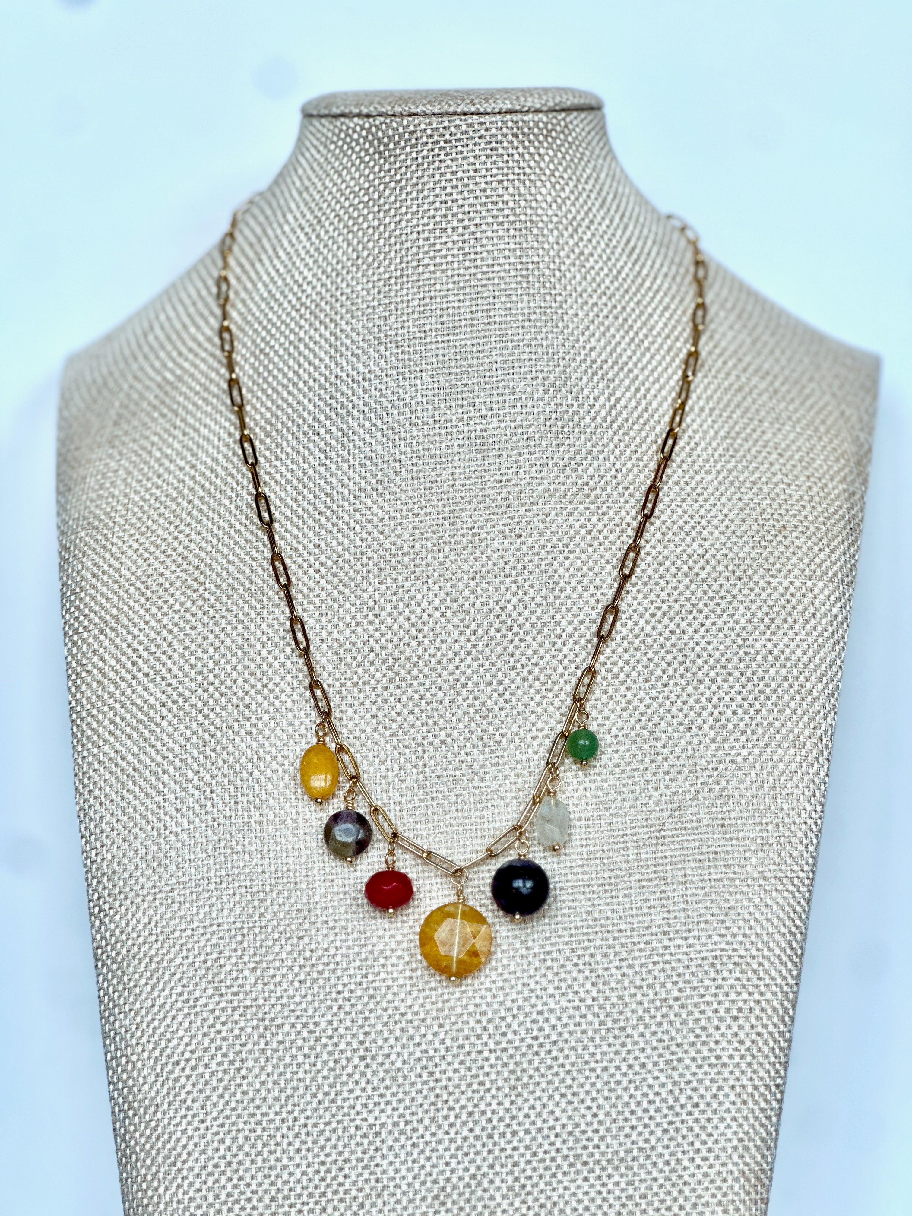 Wildflower necklace by Auréad Designs on a linen bust, front view, showing the full arrangement of seven colorful gemstone drops on a gold paperclip chain