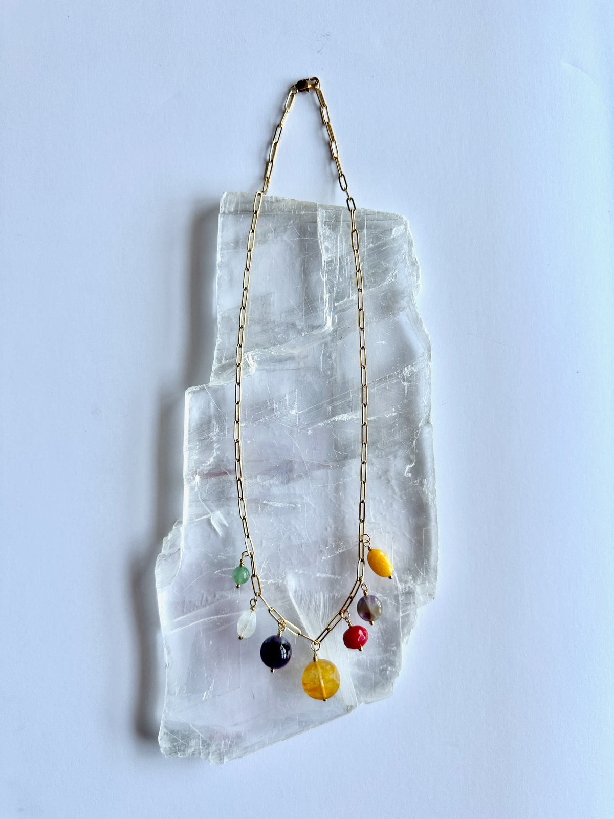 Wildflower necklace by Auréad Designs laid flat on a selenite slab, showing the full length of the gold paperclip chain with the cluster of colorful gemstone drops