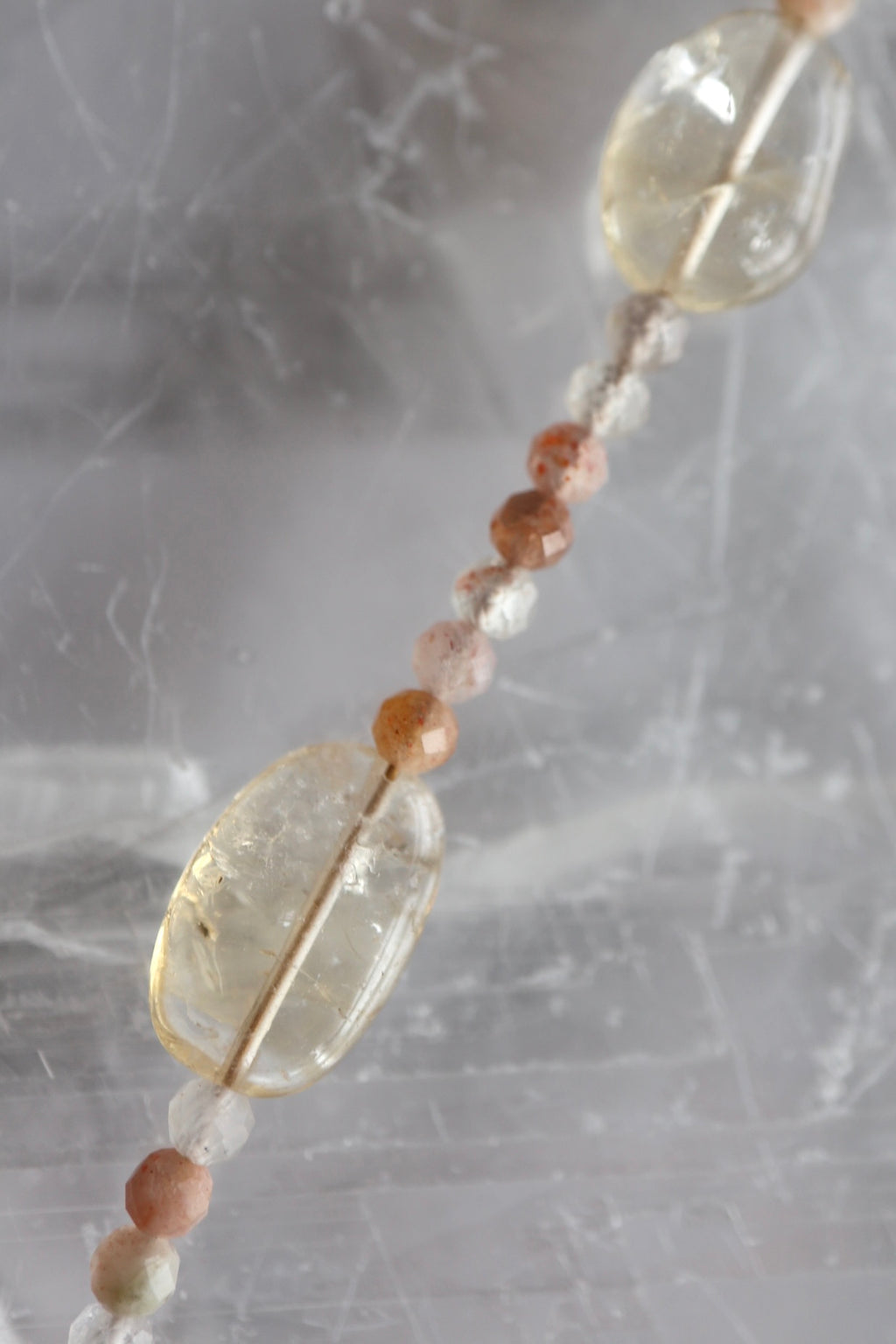 Close-up of Calora necklace showing faceted sunstone beads and polished oval citrine focal stones against a selenite background