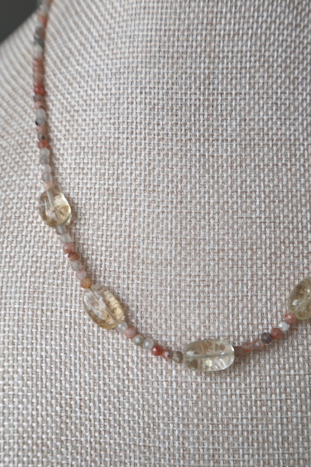 Side detail of Calora necklace on linen bust showing the mix of small faceted sunstone beads and three oval citrine focal stones with natural inclusions