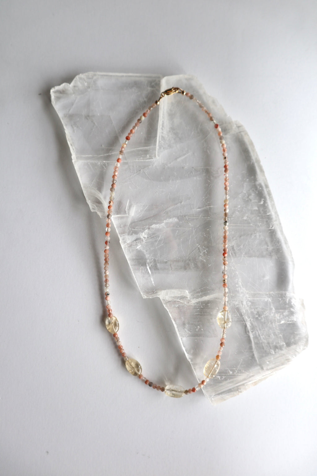 Calora sunstone and citrine necklace laid flat on a raw selenite slab, showing full length with gold-filled lobster clasp