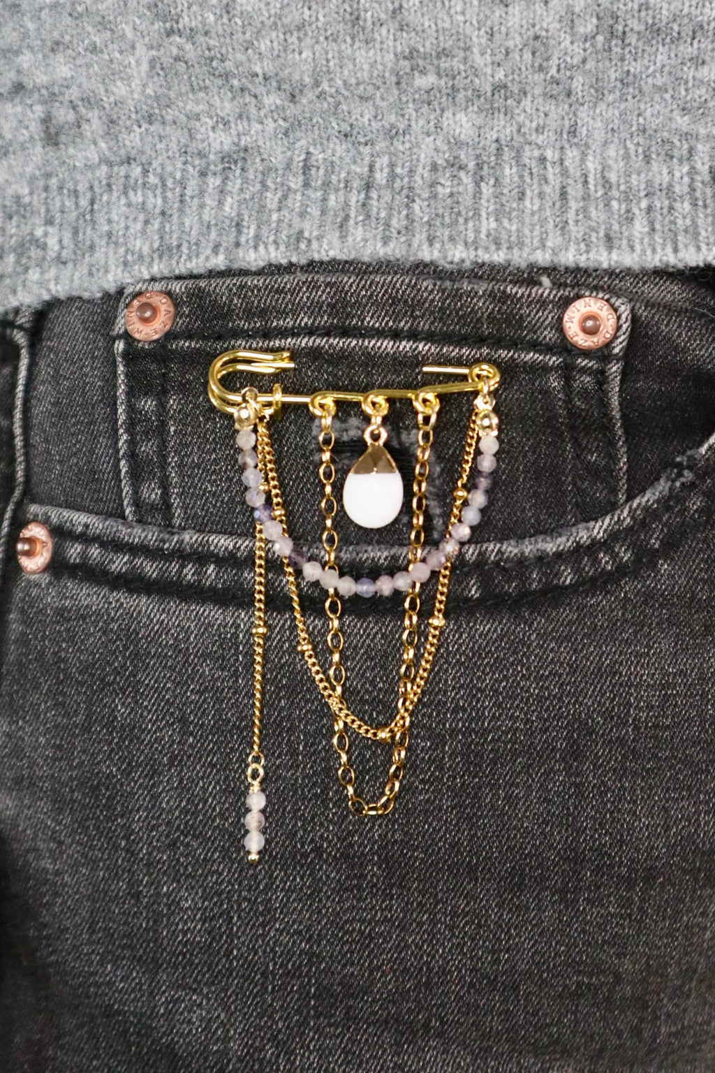 Celune iolite chain pin brooch clipped to the pocket of dark wash jeans with a grey knit top, showing a casual everyday styling option with the full chain drape visible