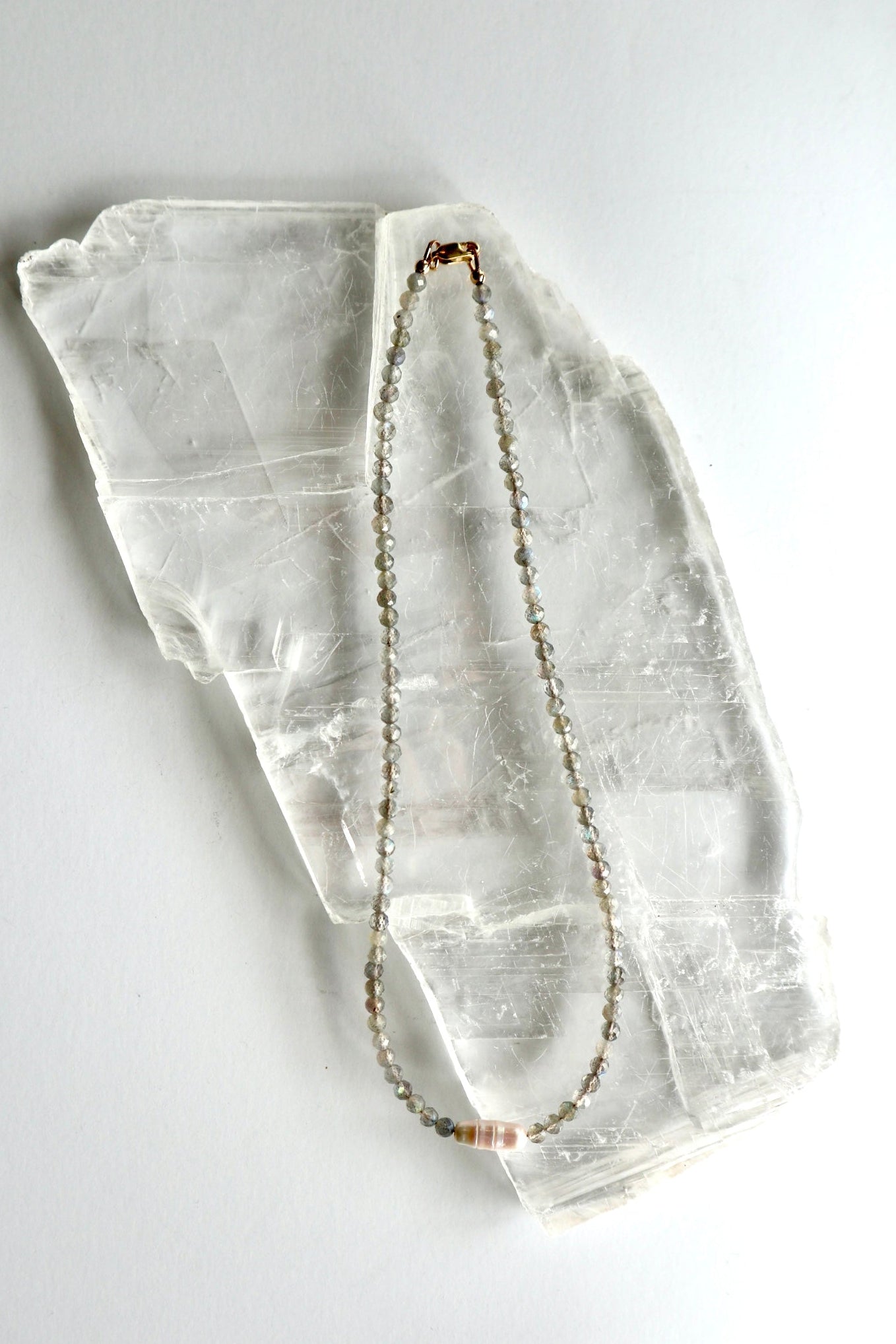 Liora labradorite and freshwater pearl necklace laid flat on a raw selenite slab, showing full collar length with gold-filled lobster clasp