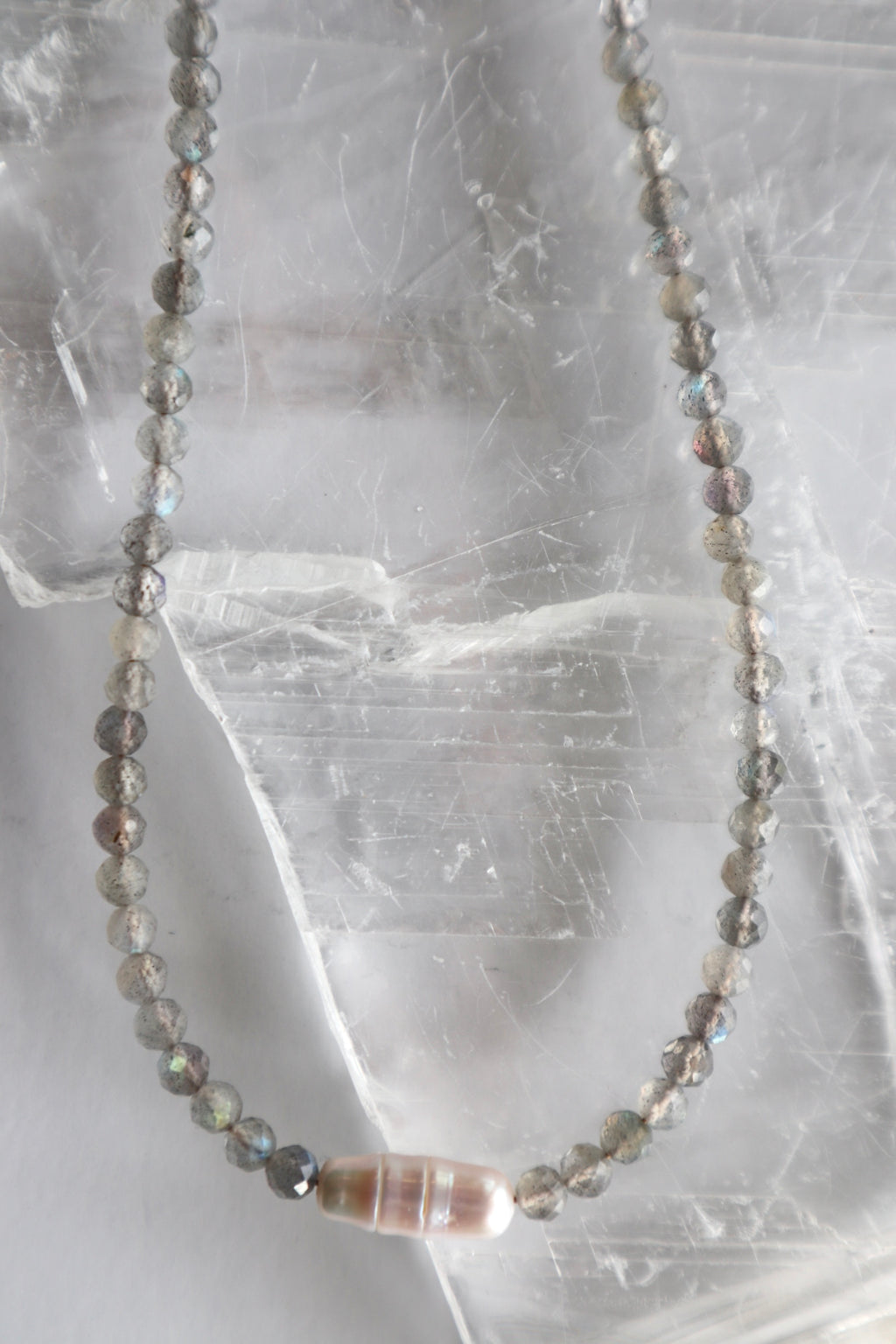 Liora necklace looped on selenite showing full strand of faceted labradorite beads with centered freshwater pearl focal piece