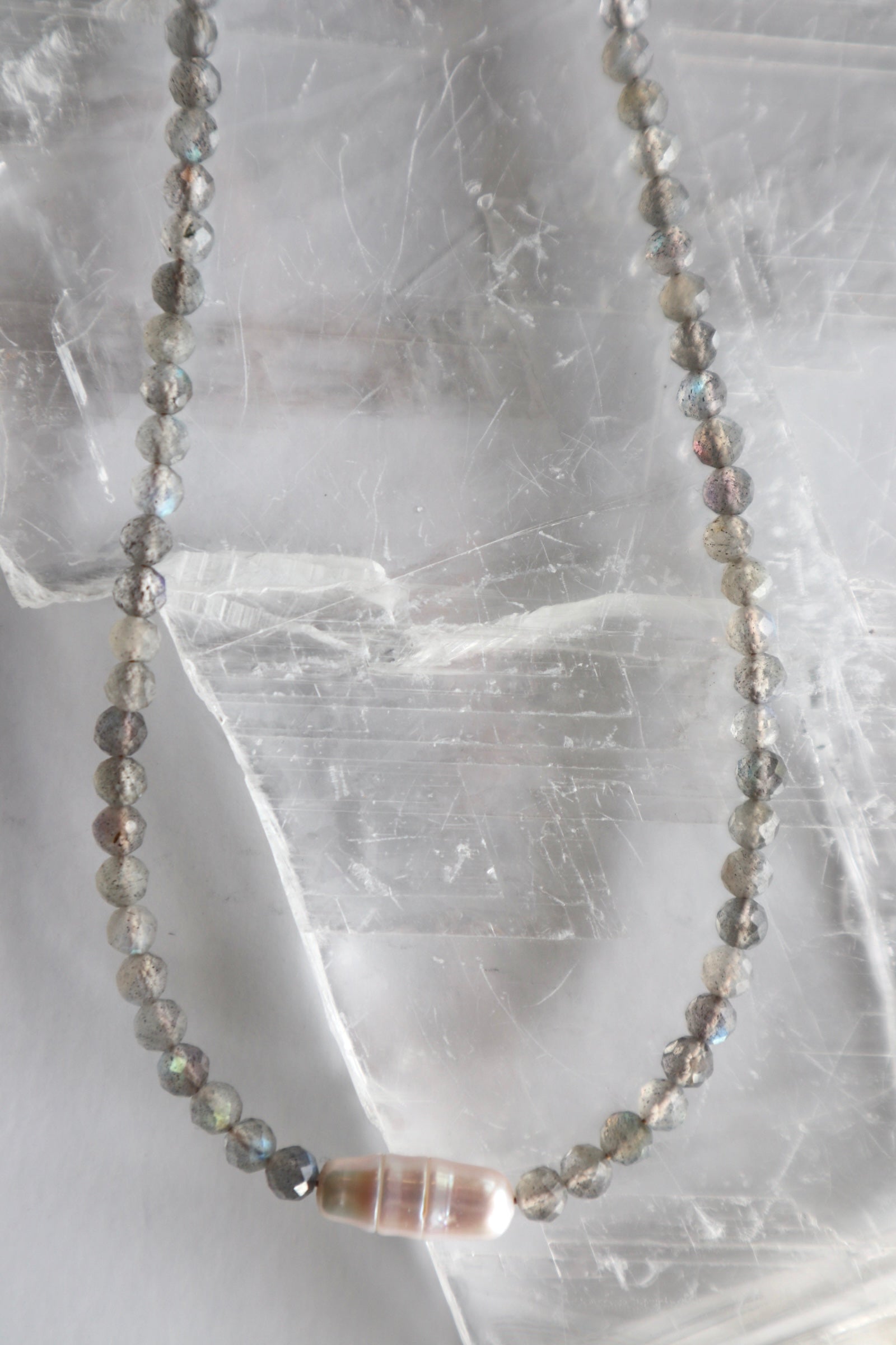 Liora necklace looped on selenite showing full strand of faceted labradorite beads with centered freshwater pearl focal piece