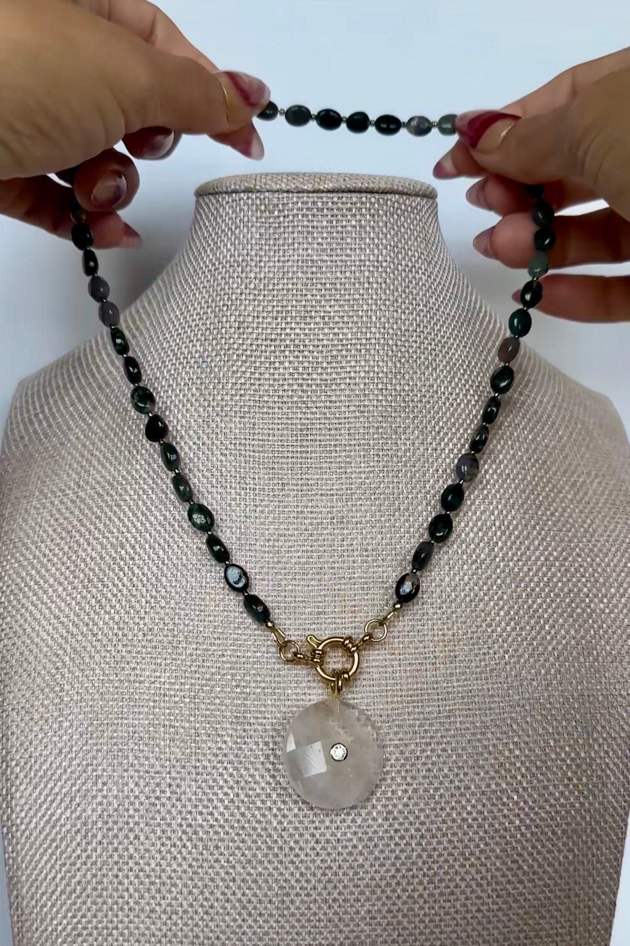 Video of the Trail necklace by Auréad Designs, featuring moss agate oval beads and a clear quartz donut pendant with a gold ring clasp, shown in full, styled on a linen bust, and worn