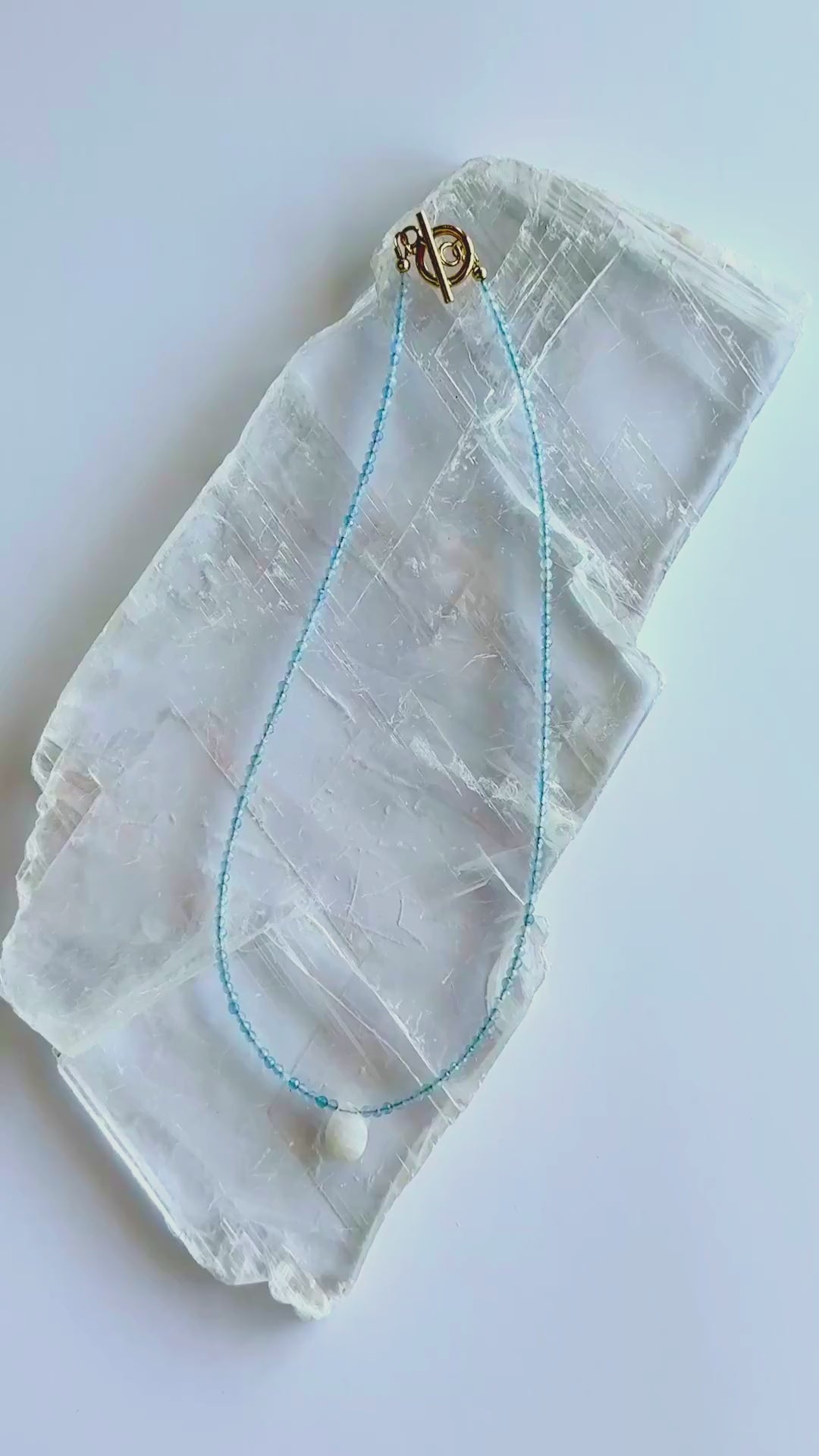Auréad Designs Marevane necklace with faceted natural aquamarine beads and rainbow moonstone teardrop pendant shown in motion with gold toggle clasp.