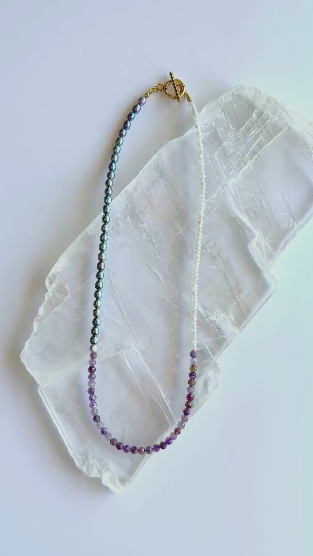 Auréad Designs Irisenne necklace with faceted amethyst beads, peacock green freshwater pearls, and rainbow moonstone rondelles shown in motion with gold toggle clasp.