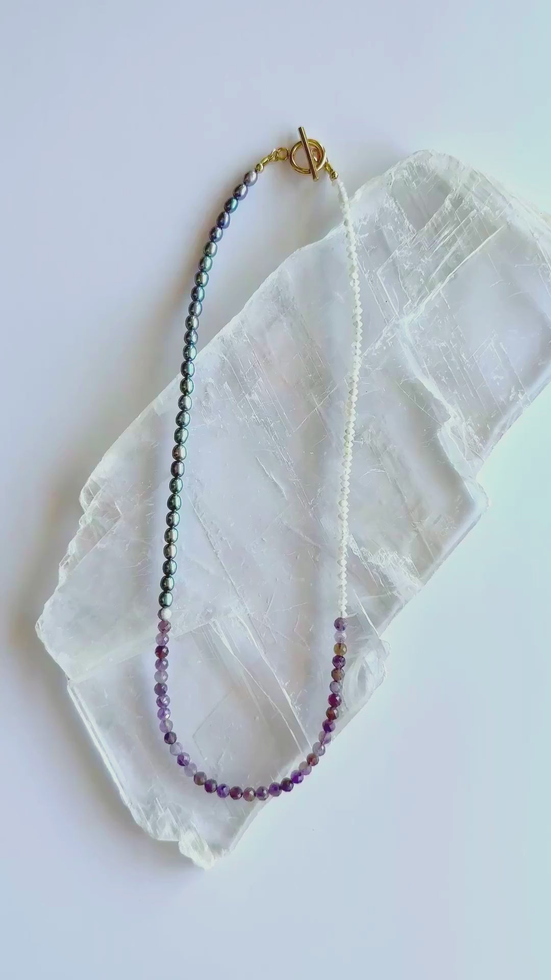 Auréad Designs Irisenne necklace with faceted amethyst beads, peacock green freshwater pearls, and rainbow moonstone rondelles shown in motion with gold toggle clasp.